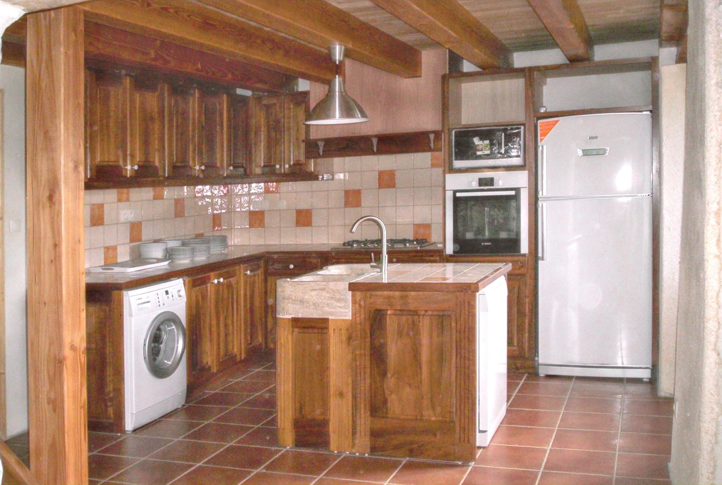 Una cocina con armarios de madera, lavadora, pileta, refrigerador y salpicadero de azulejos.