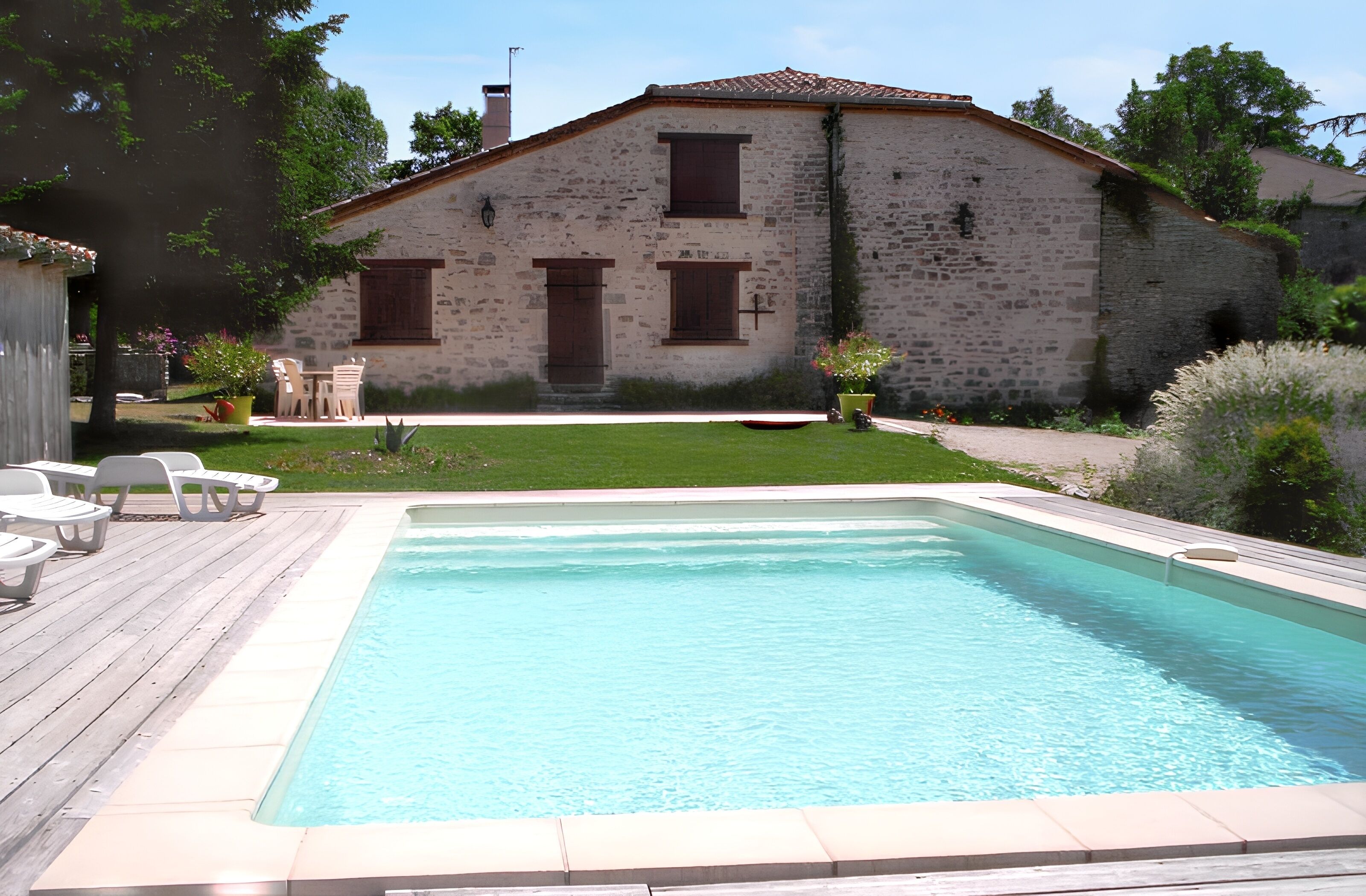 A stone building with a swimming pool, outdoor seating, and a well-maintained lawn.