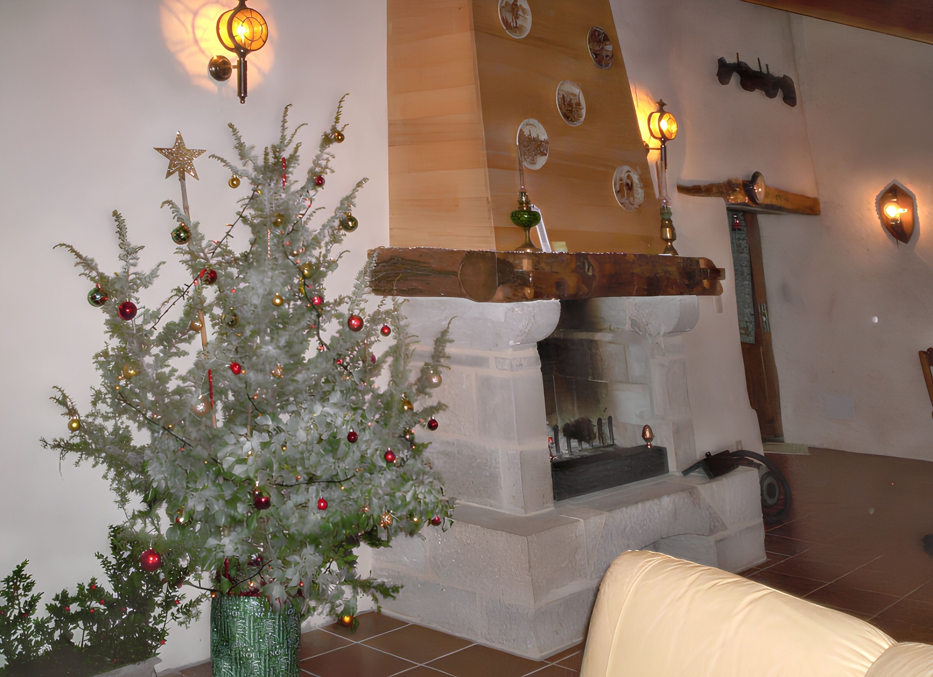 Een kerstboom versierd met decoraties, een open haard en wandlampen.