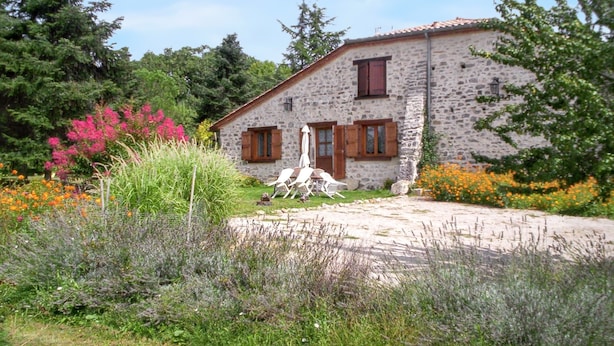 Una casa de piedra con jardín, camino de entrada pavimentado y mobiliario exterior.