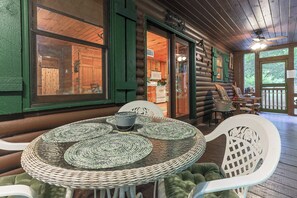 Uma cabana de toras com área de jantar, destacando uma mesa redonda com jogos americanos trançados e cadeiras brancas.