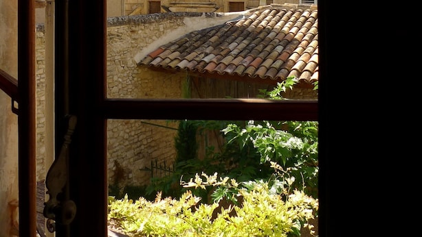 A view through an open window of a building with a bell tower, a circular window, and a stone wall. - Live a unique 'provencale' experience in the heart of the Luberon (Apt)
