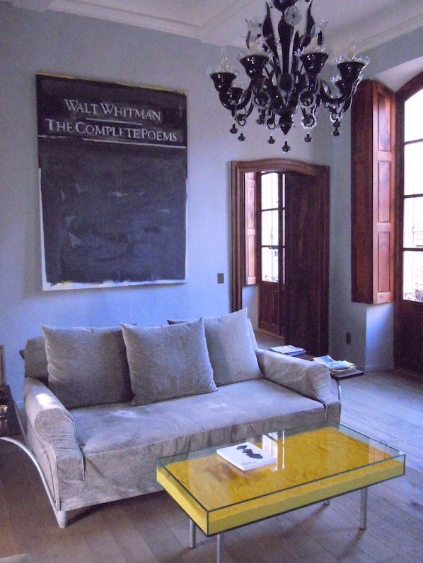 A room with a sofa, a glass coffee table, a chandelier, and a wall-mounted book titled "Walt Whitman The Complete Poems".