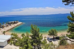 Ett kustområde med en strand, klart blått hav och några parkerade bilar.