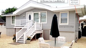 Une maison avec un porche à l’avant, un escalier, un coin repas avec une table et des chaises, et un parapluie noir.
