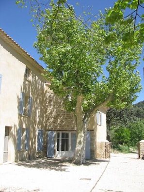 Un bâtiment de style architectural traditionnel, caractérisé par une façade en pierre et un grand arbre qui se trouve devant.