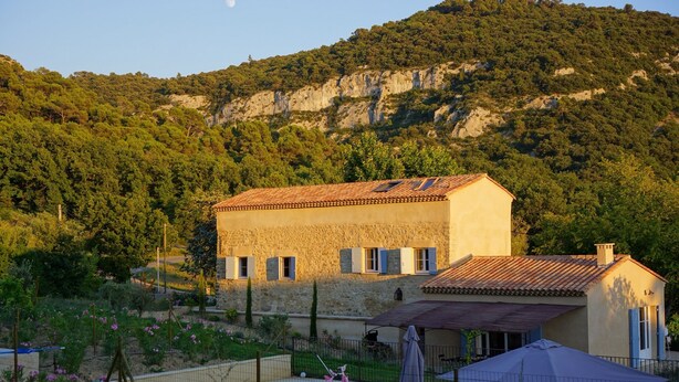 A stone building with a tiled roof, surrounded by a swimming pool and garden.