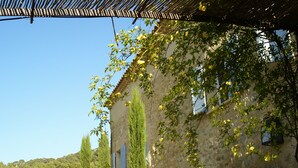 A stone building with a rustic charm, featuring a wooden pergola and lush greenery.