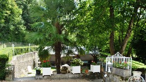 Eine Gartenpatio mit Kiesboden, weißen Metallstühlen und verschiedenen Blumentöpfen.