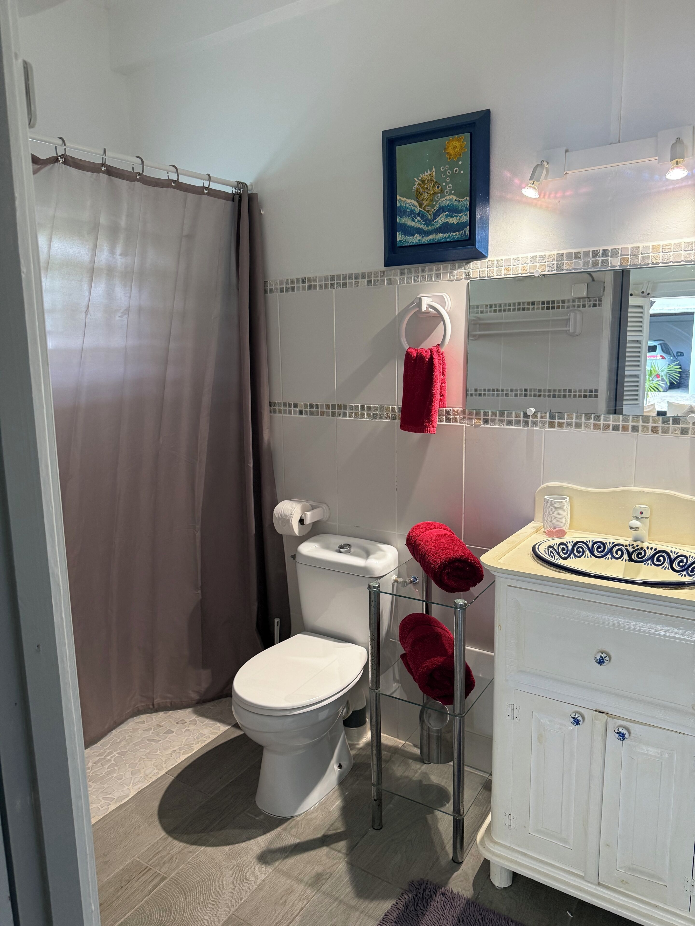 A bathroom with a toilet, a glass shower enclosure, a sink with a mirror, and a towel rack with red towels.