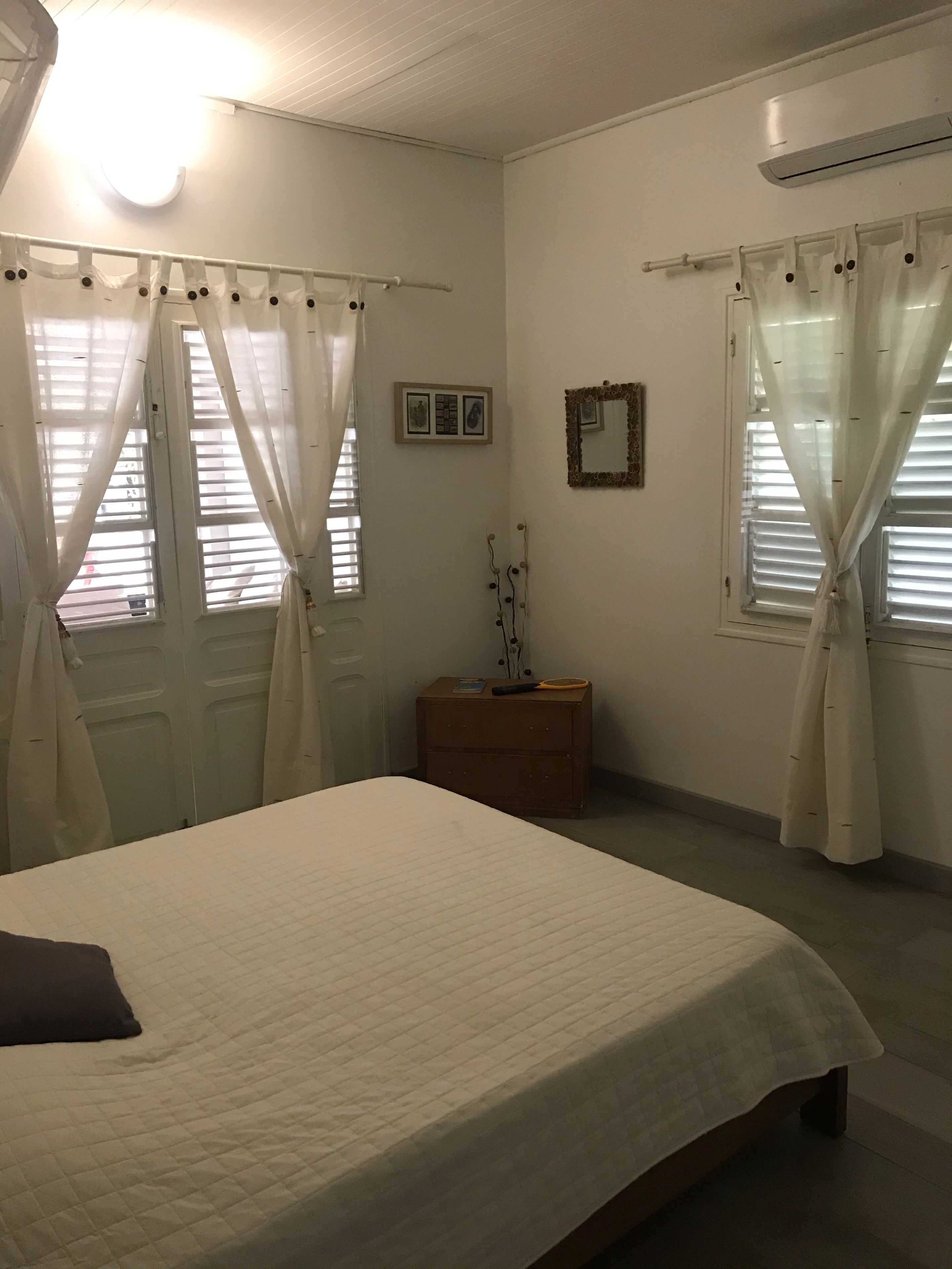 A bedroom with a bed, a nightstand, a mirror, and curtains on the windows.