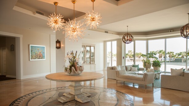 A spacious living room with a round coffee table, two sofas, and a large window offering a view of palm trees.