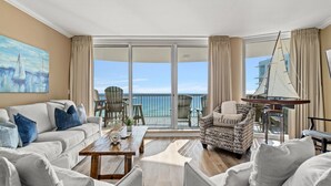 A spacious living room with a sofa, armchairs, a coffee table, and a balcony with a view of the sea.