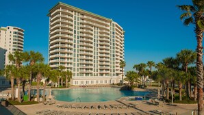 A large hotel with a pool area, multiple balconies, and palm trees.