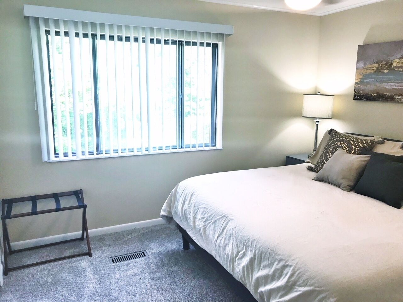 Une chambre à coucher avec un lit, une fenêtre avec des stores, une lampe de chevet et un tableau au mur.