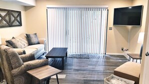 A living room with a sofa, a coffee table, a TV, and a sliding glass door with blinds.