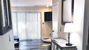 A compact living space with a kitchenette, a dining area, and a large window with blinds.