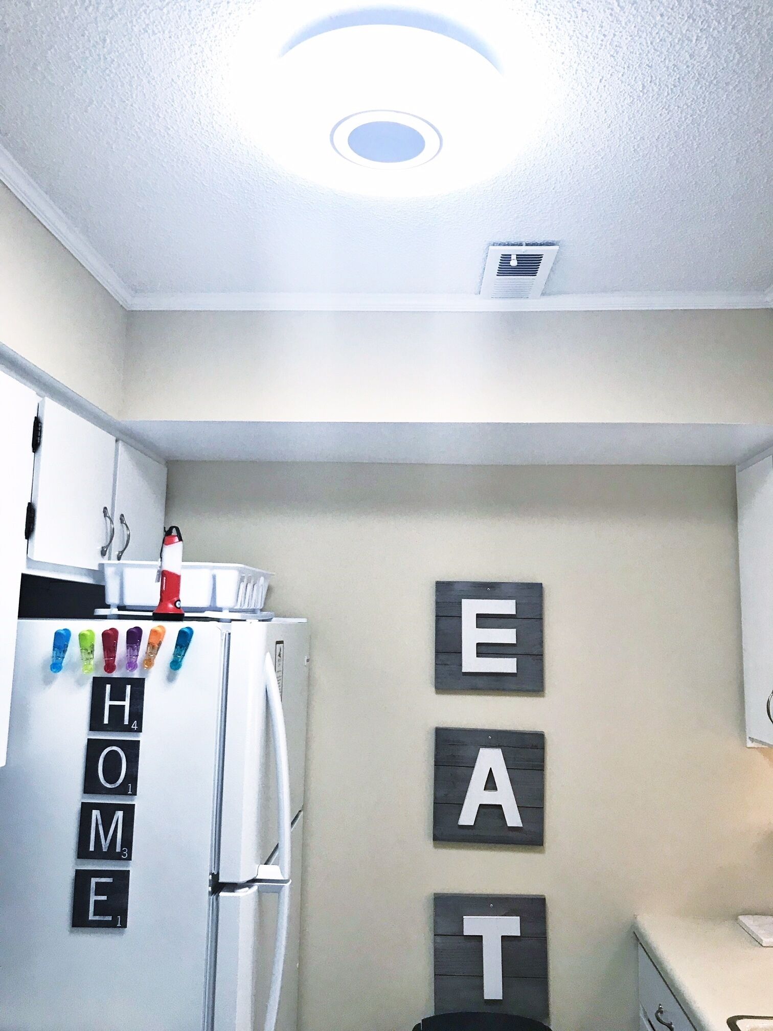 A kitchen with a refrigerator, a sink, and cabinets. There are letters spelling 'HOME' on the wall.