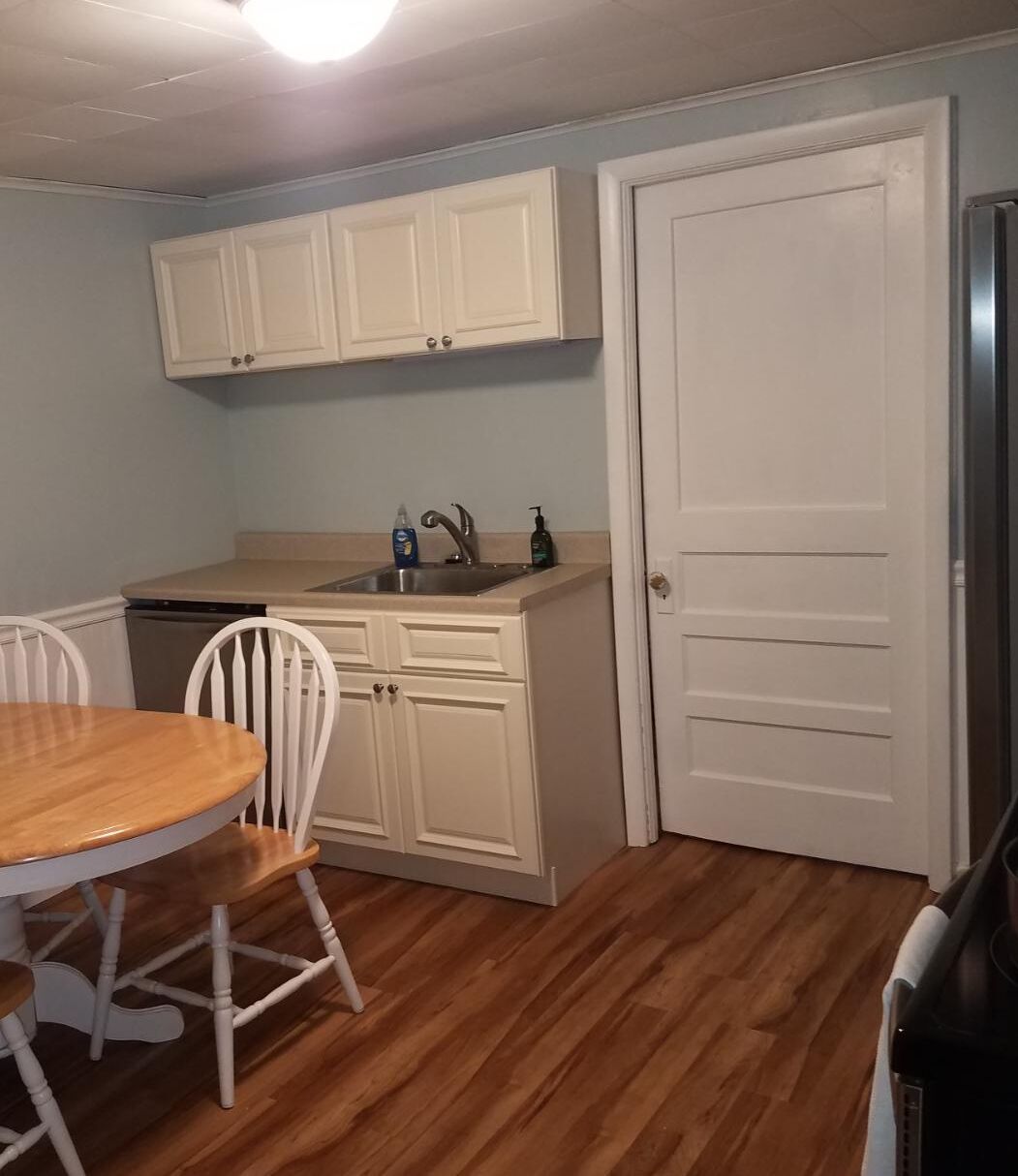 A compact kitchen with white cabinets, a sink, and a dining area with a wooden table and white chairs.