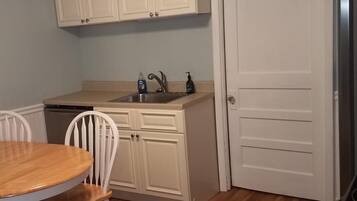 A compact kitchen with white cabinets, a sink, and a dining area with a wooden table and white chairs.