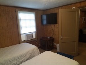 Una habitación de hotel con dos camas, un televisor fijado a la pared y una ventana con persianas.