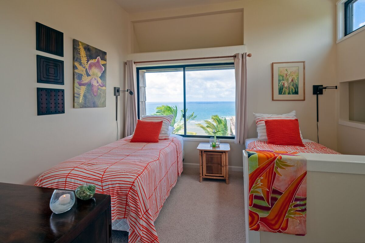 Habitación de hotel con dos camas, una mesita pequeña y ventana con vista al océano.