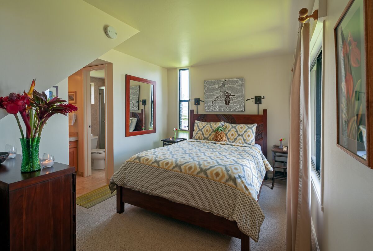 A bedroom with a bed, a bedside table, a nightstand, a mirror, and a door leading to the bathroom.