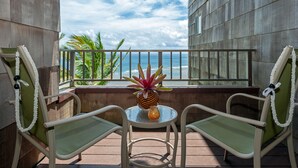A balcony with two chairs and a small table, overlooking the ocean.