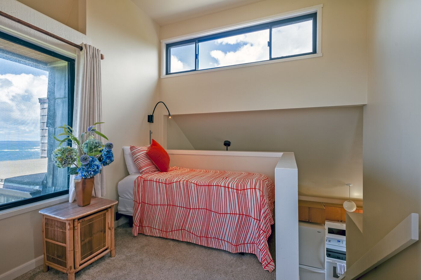 A bedroom with a bed, a window, a small table with a plant, and a ceiling light.