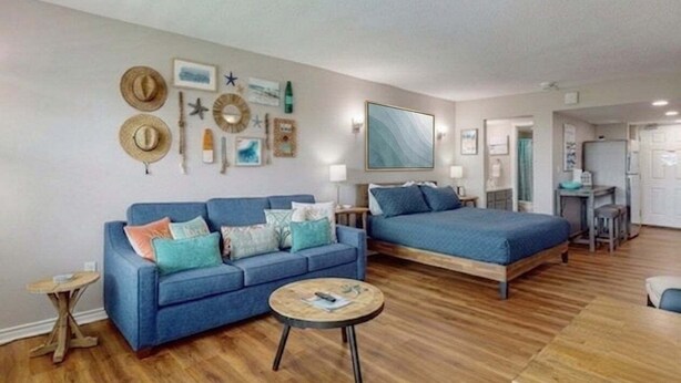 Una habitación con un sofá azul, una cama, una mesa de centro redonda y una pared decorada con sombreros y estrellas de mar.