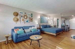 Une pièce avec un canapé bleu, un lit, une table basse ronde et un mur décoré de chapeaux et d’étoiles de mer.