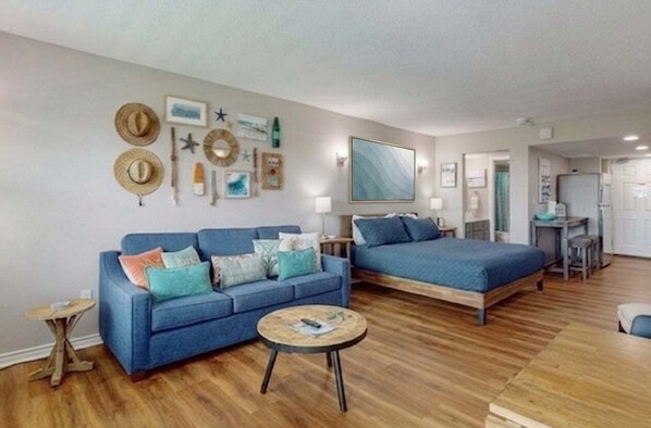 Ein Zimmer mit einem blauen Sofa, einem Bett, einem runden Couchtisch und einer Wand, die mit Hüten und Seesternen dekoriert ist.