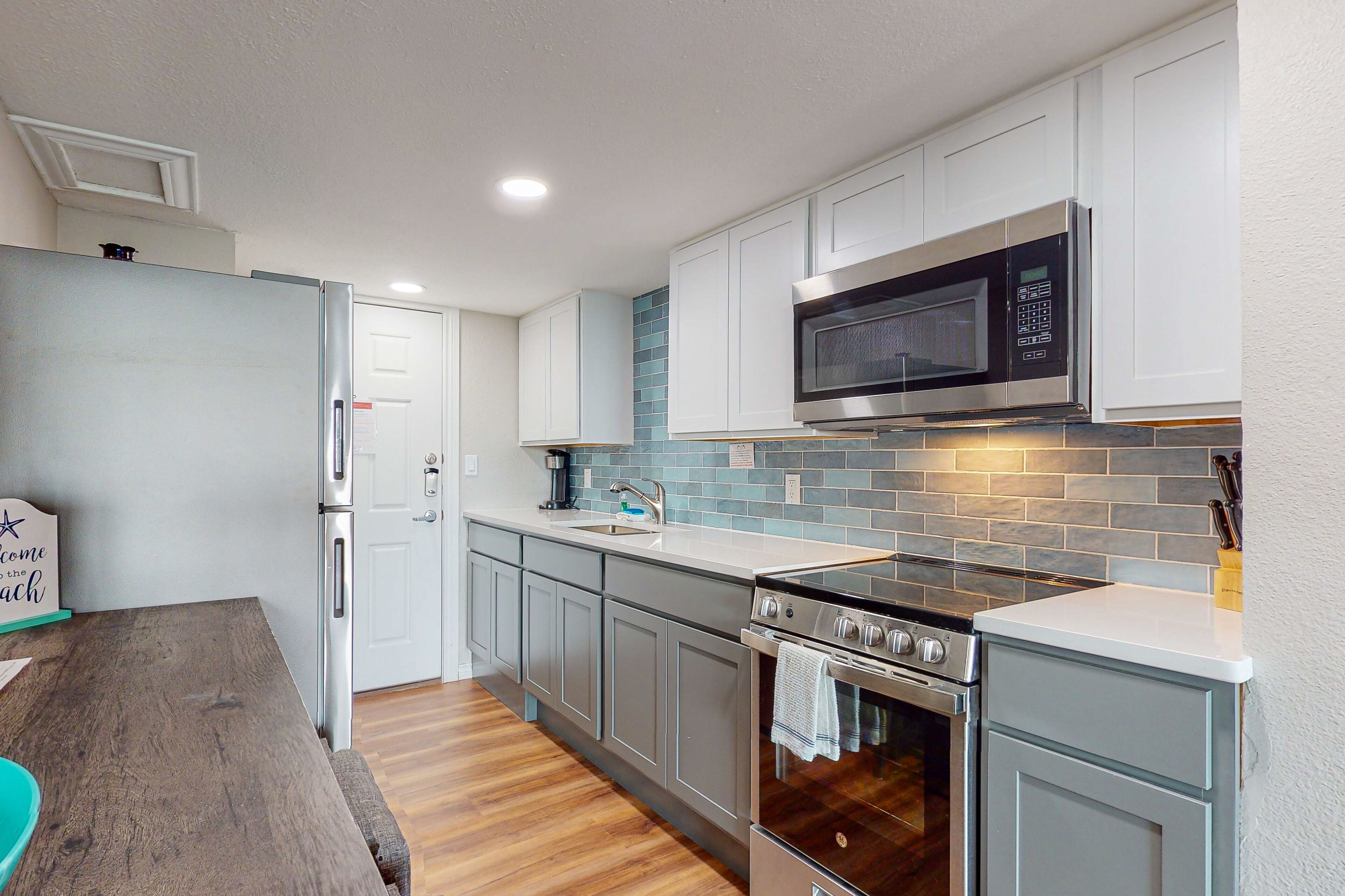 A modern kitchen with white cabinets, a stainless steel microwave, a built-in oven, and a wooden dining table.