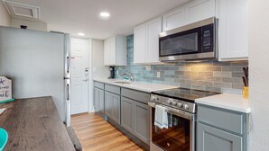 Una cocina moderna con armarios blancos, un microondas de acero inoxidable, un horno empotrado y una mesa de comedor de madera.