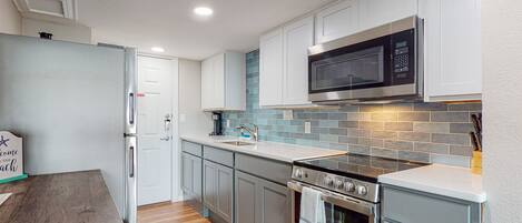 A modern kitchen with white cabinets, a stainless steel microwave, a built-in oven, and a wooden dining table.