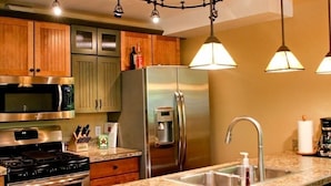 A modern kitchen with stainless steel appliances, wooden cabinets, and pendant lighting.
