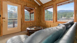 Una habitación con paredes de madera, un sofá de cuero, una mesa de vidrio y ventanas amplias con vistas a la montaña.