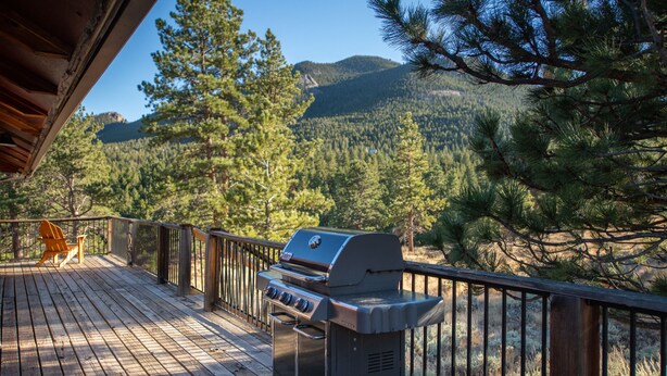 Una terraza con una parrilla, cubierta de madera y vistas a una montaña boscosa.