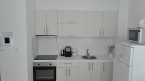 Eine kompakte Küche mit weißen Schränken, einer Mikrowelle, einer Kaffeemaschine und einem Spülbecken.