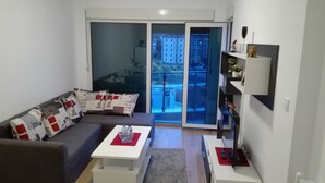 Ein modernes Wohnzimmer mit einer Couch, einem Couchtisch und einem Fernseher. Eine Glastür führt zu einem Außenbalkon.