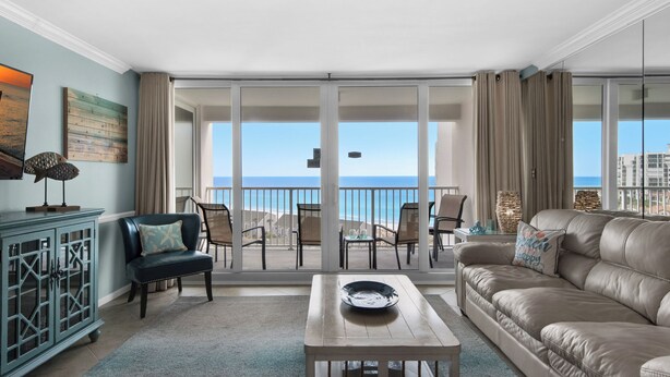 A spacious living room with a large sliding glass door leading to a balcony with a view of the ocean. There is a leather sofa, a wooden coffee table, and a blue armchair. - 🌅 Gulf-View Condo | Seasonal Beach Service Included | Shoreline 3104 (Destin)
