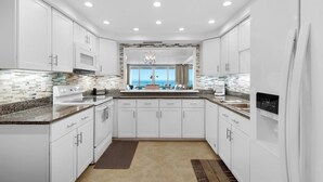 A modern kitchen with white cabinets, granite countertops, and a large window with a view. - 🌅 Gulf-View Condo | Seasonal Beach Service Included | Shoreline 3104 (Destin)