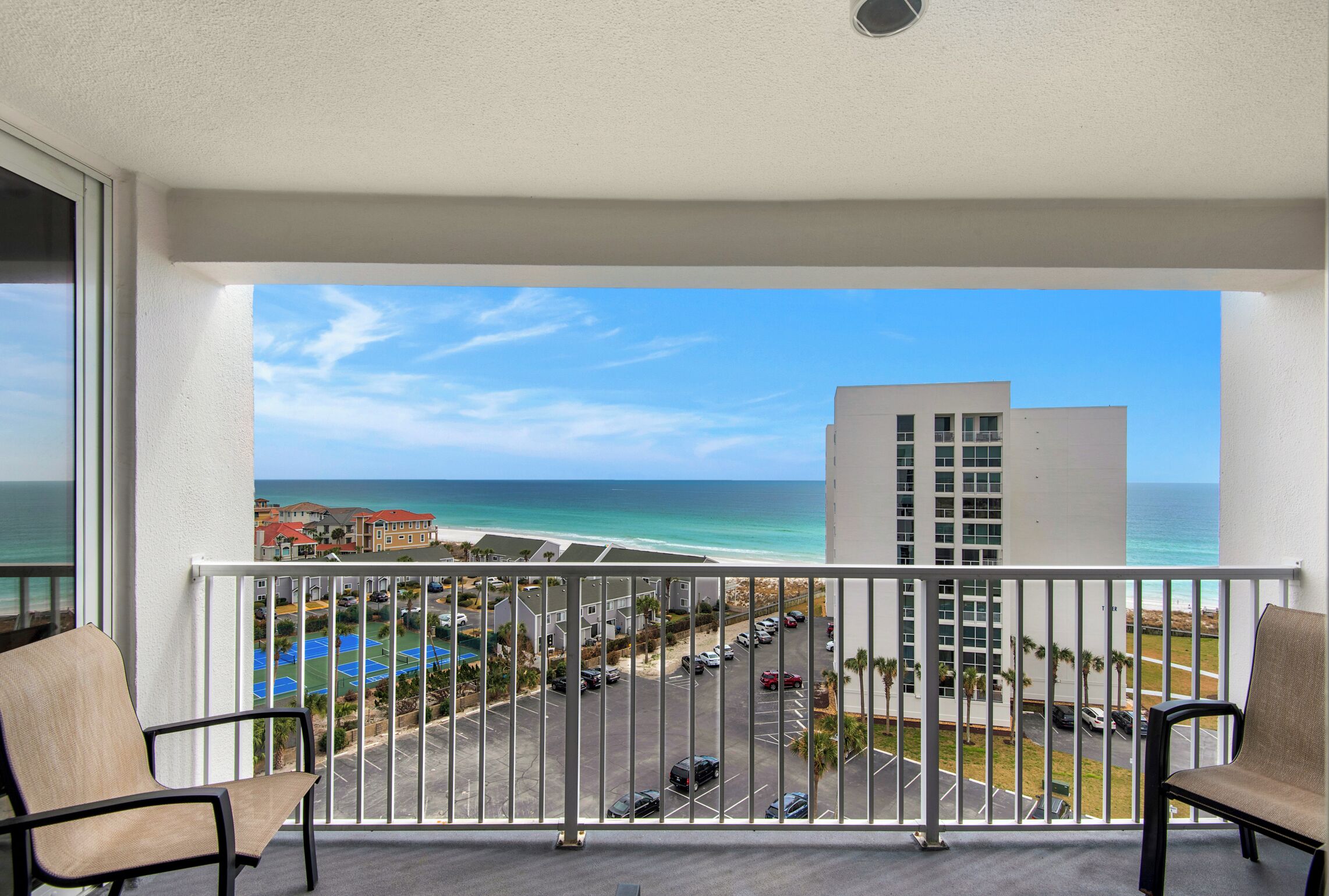 A balcony with a view of the ocean and a parking lot.