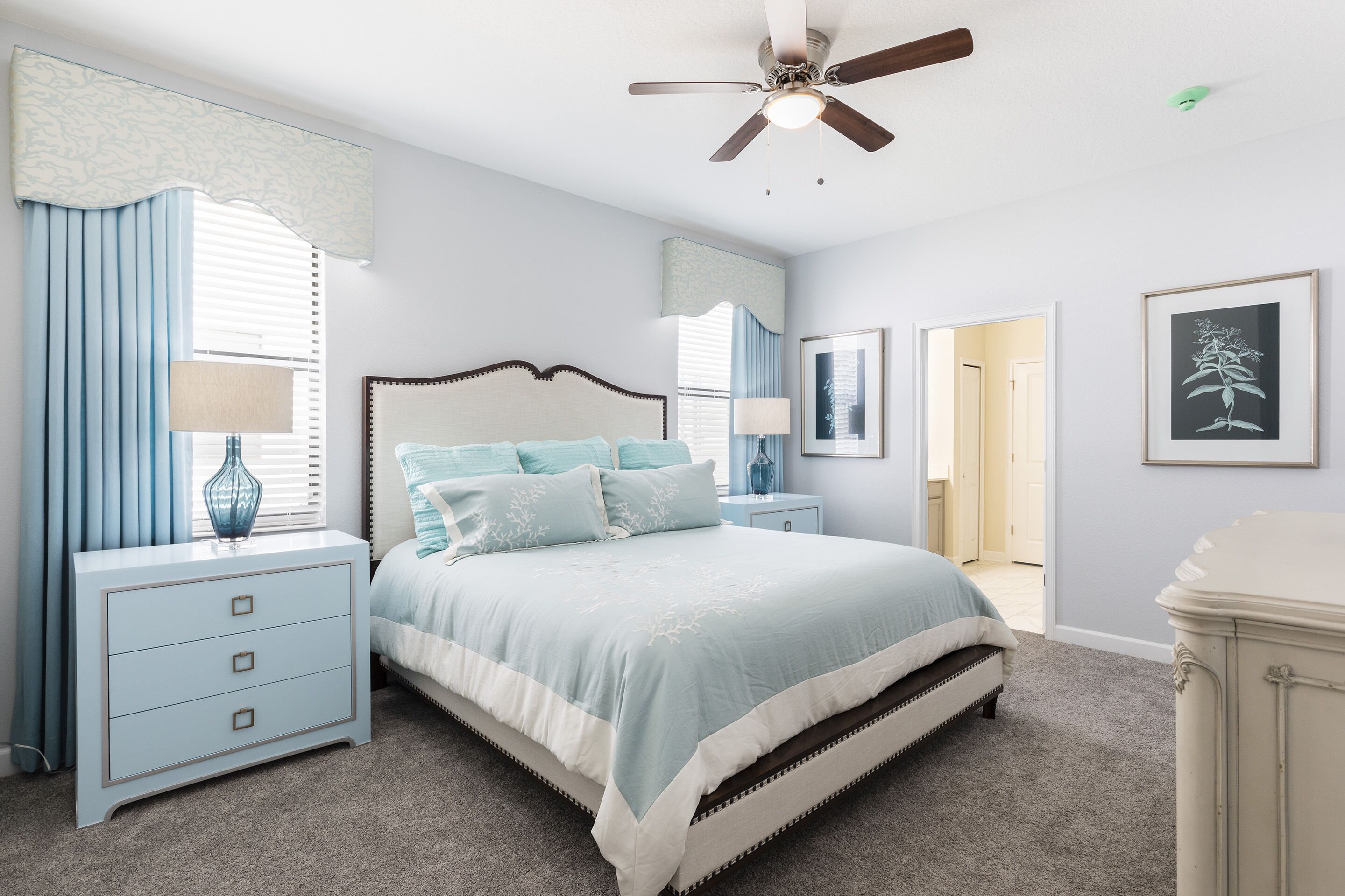 A bedroom with a bed, nightstands, a dresser, a ceiling fan, and a door leading to another room.