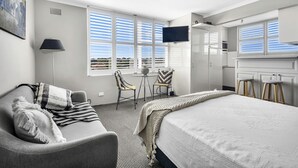 Une chambre d’hôtel comprenant un lit, un canapé, une télévision, un bureau avec une chaise et une fenêtre avec des stores.