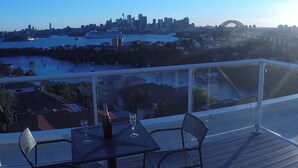 Un balcon avec une table et des chaises donnant sur une vue panoramique de la ville, avec un pont particulièrement imposant.