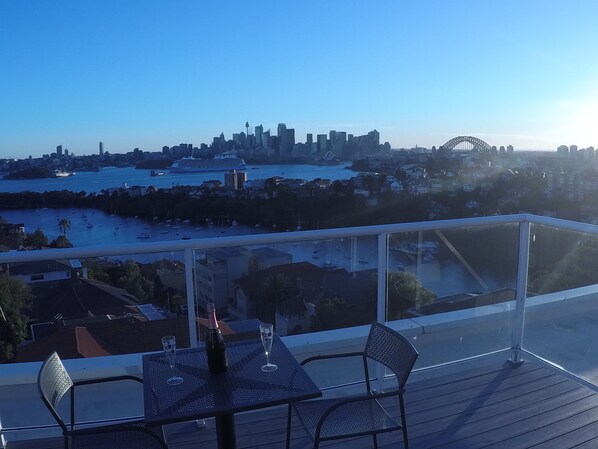 A balcony with a table and chairs overlooking a cityscape with a prominent bridge.