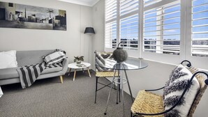 Un salon moderne avec un canapé gris, une table ronde en verre et une vue sur la ville grâce à de grandes fenêtres.