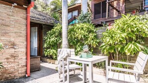 Un patio con mesa y sillas, rodeado de abundante vegetación y un edificio de madera.