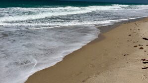Una playa con olas, cielo despejado y huellas en la arena.